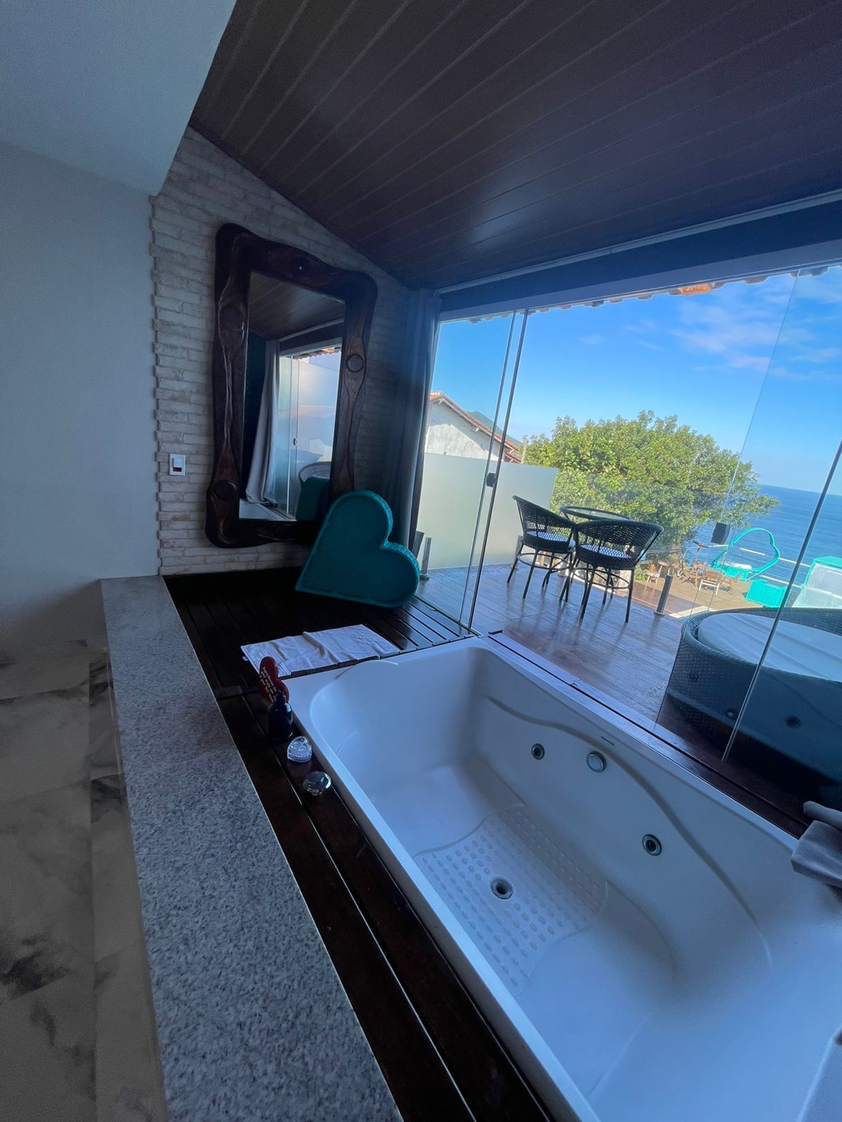 A modern bathroom with a large bathtub, a wooden vanity, and a view of the ocean through large windows.