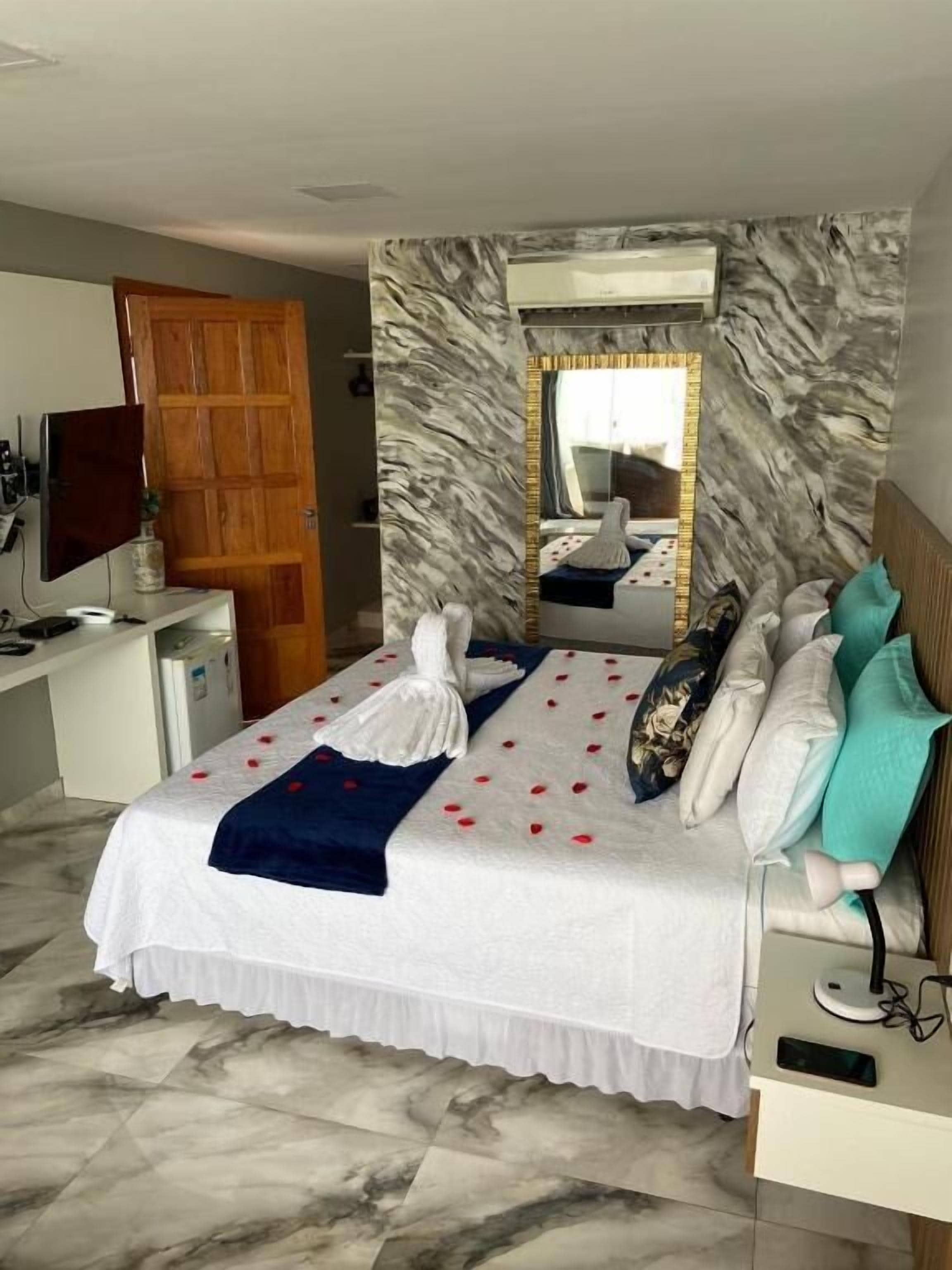 Ett hotellrum med en säng, ett skrivbord, en tv och en spegel.