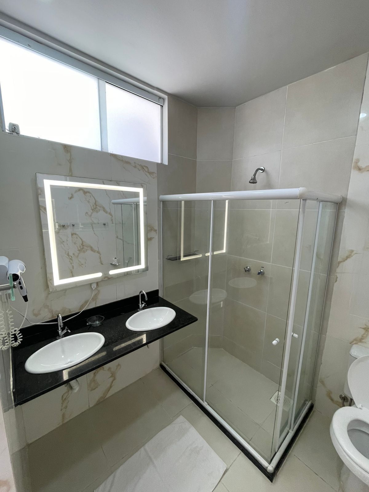 A modern bathroom with two sinks, a glass shower enclosure, and a toilet.