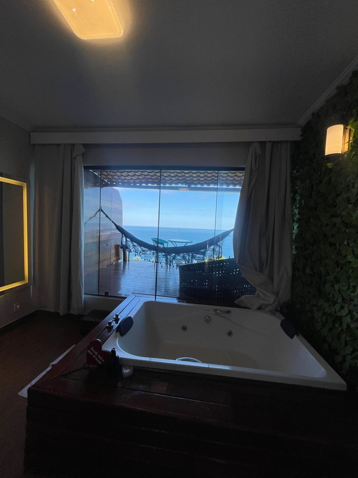 A room with a large window, a jacuzzi, and a view of the sea.