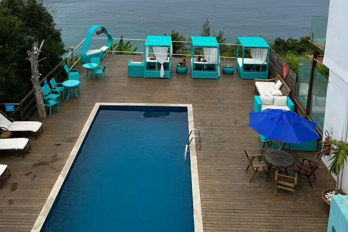 Area piscina con vista sul mare, prendisole in legno e sedie a sdraio color turchese.