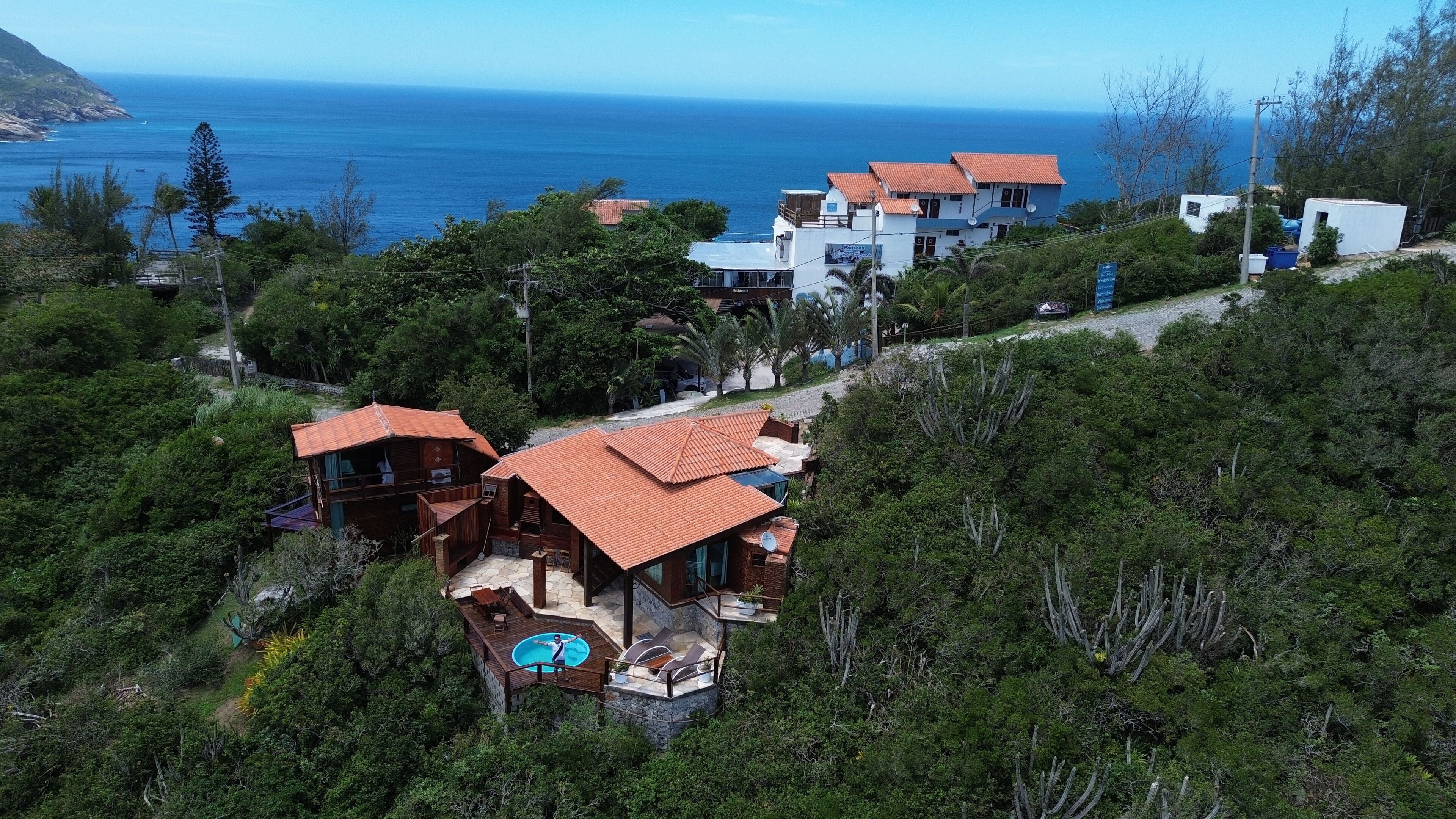 Una propiedad en una colina con varias construcciones, piscina y vista al océano.