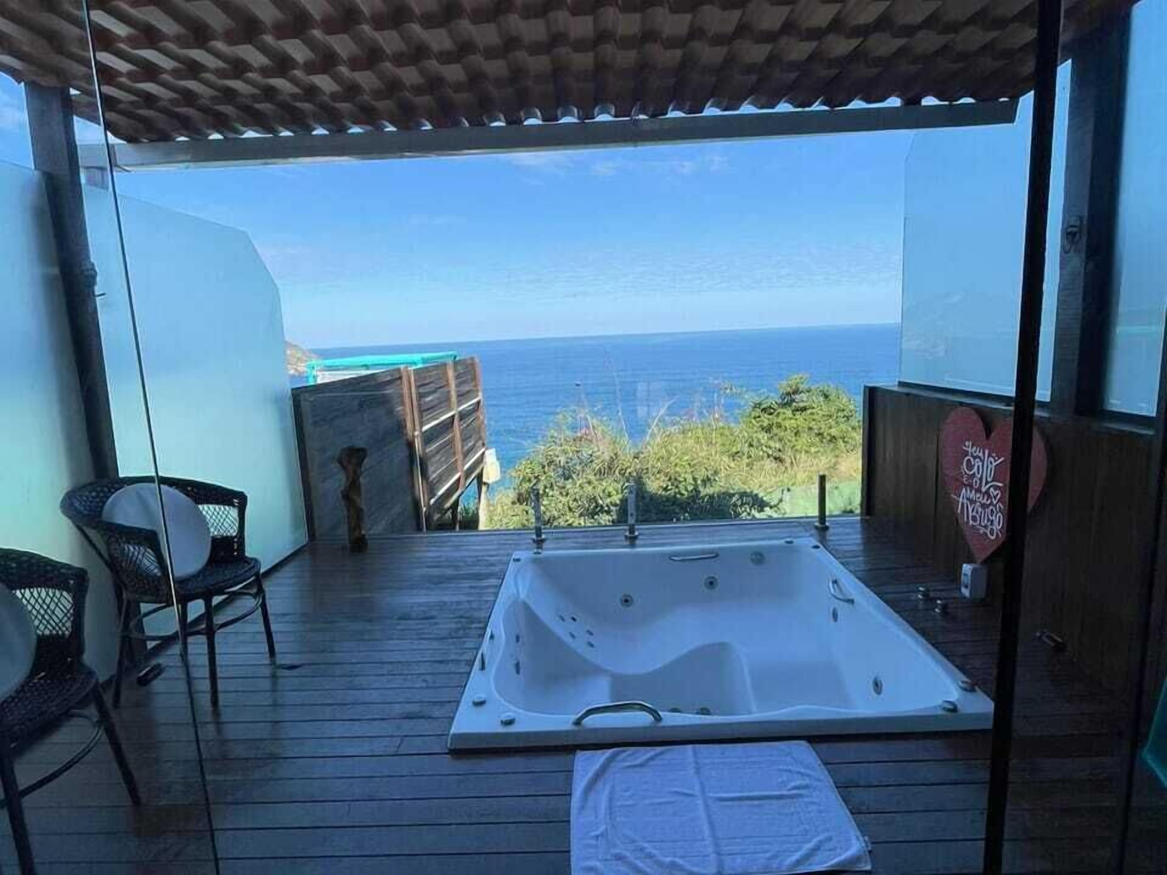 A wooden deck with a hot tub, chairs, and a view of the sea.