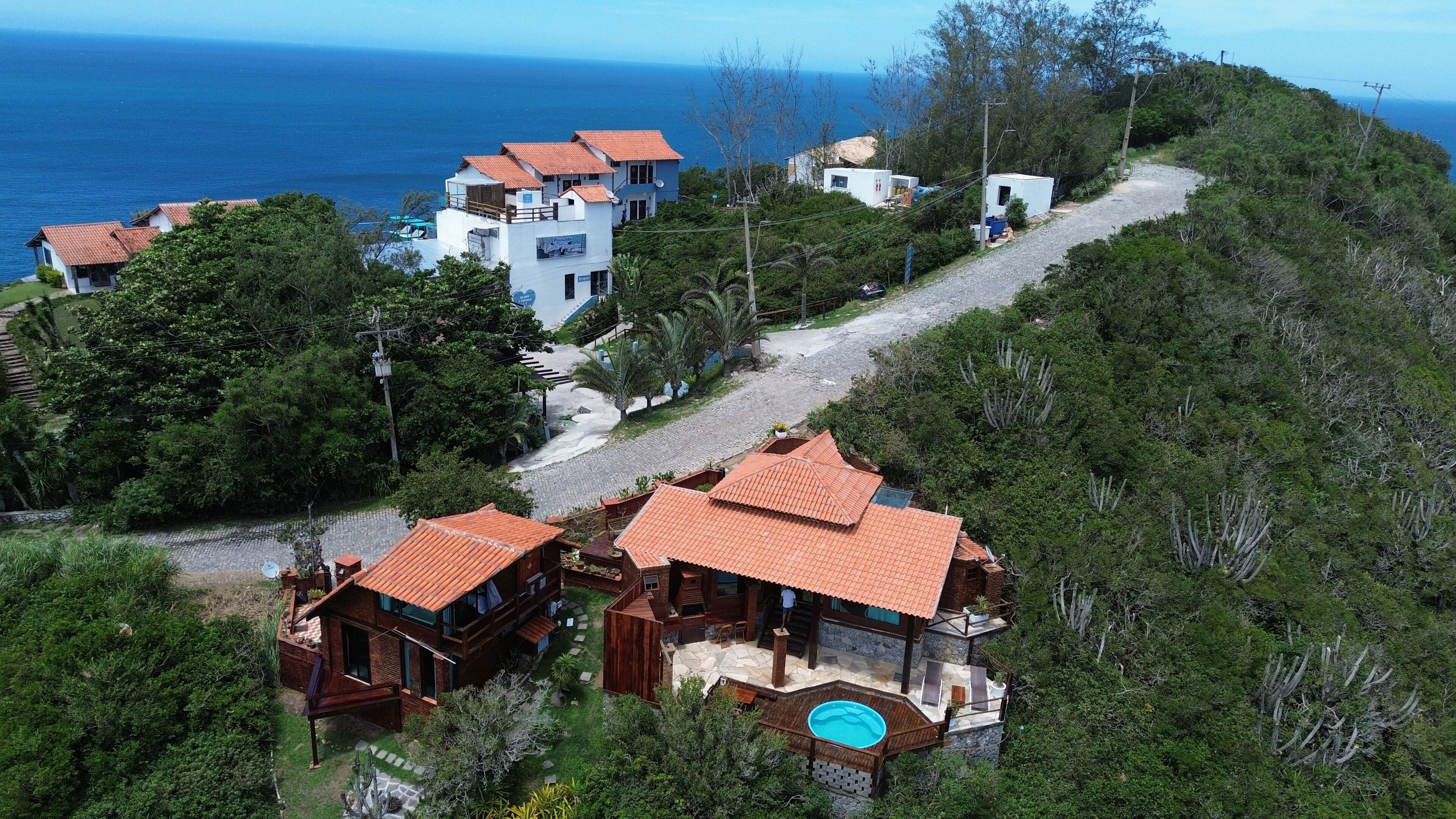 A hillside property with multiple buildings, a swimming pool, and a view of the ocean.