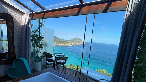 Une chambre moderne dotée d’une grande baignoire, d’un coin repas avec des chaises et une table, et offrant une vue sur la mer.