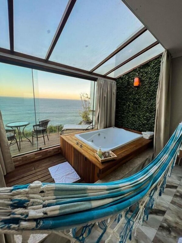 A room with a wooden deck, a large window overlooking the sea, a wooden bathtub, and a hammock. - Pousada e Restaurante Vista Turquesa (Arraial do Cabo)