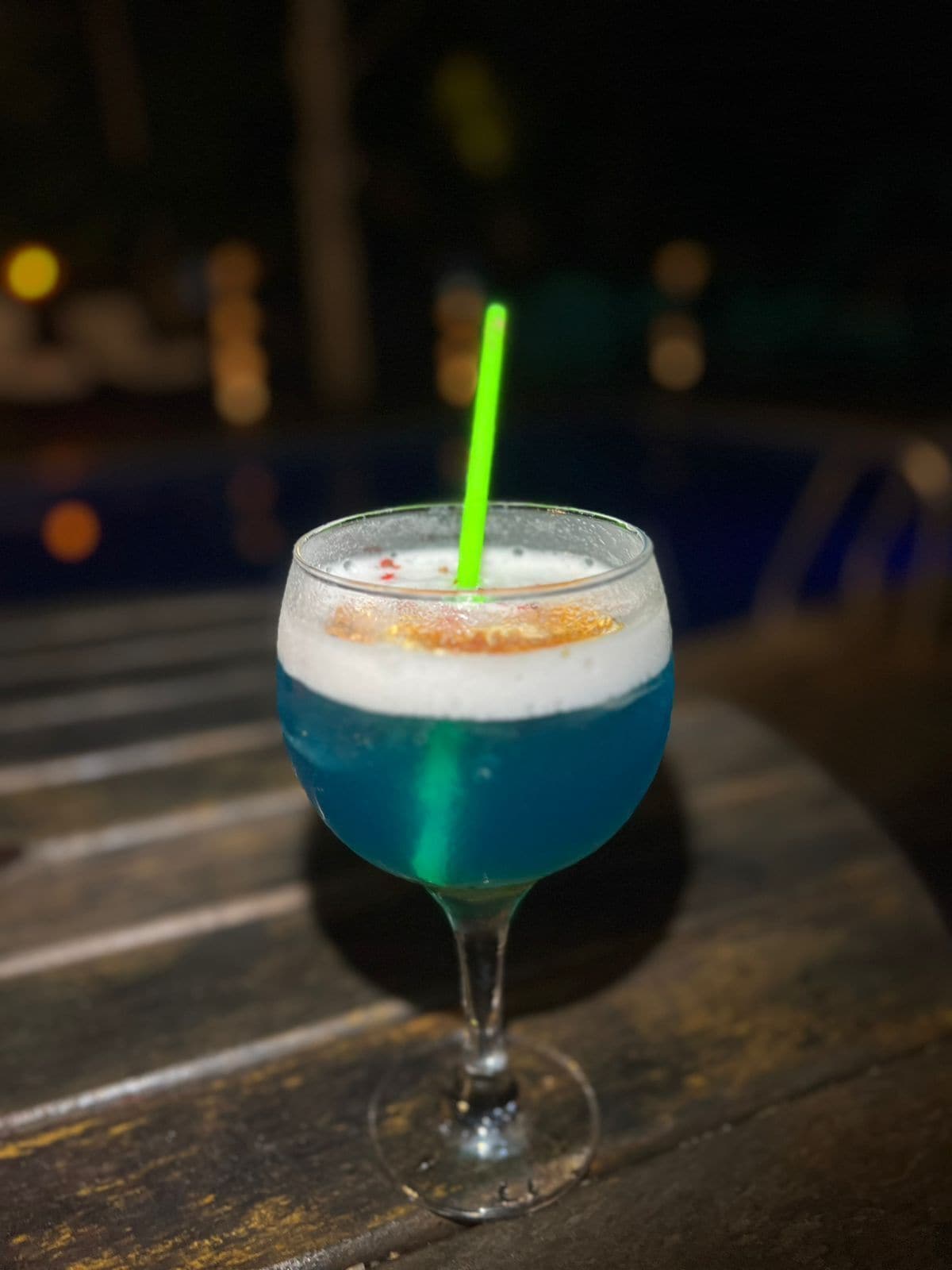 Un cóctel en un vaso con una pajita verde sobre una mesa de madera.