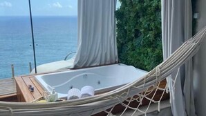 Un fauteuil suspendu au-dessus d’un sol en marbre, une baignoire et une vue sur la mer.