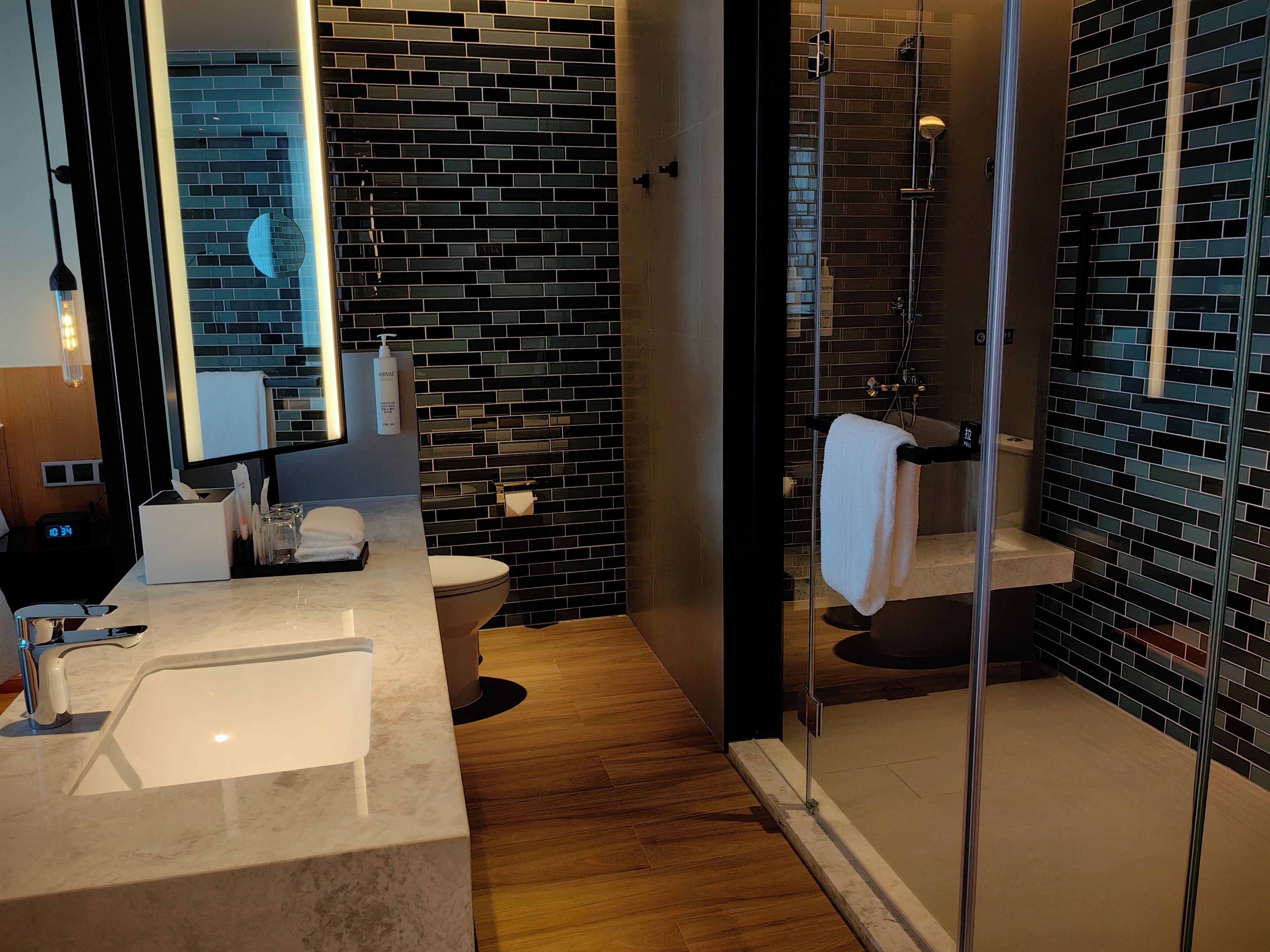 Um banheiro moderno com pia de mármore, box de vidro e parede revestida de azulejos pretos.