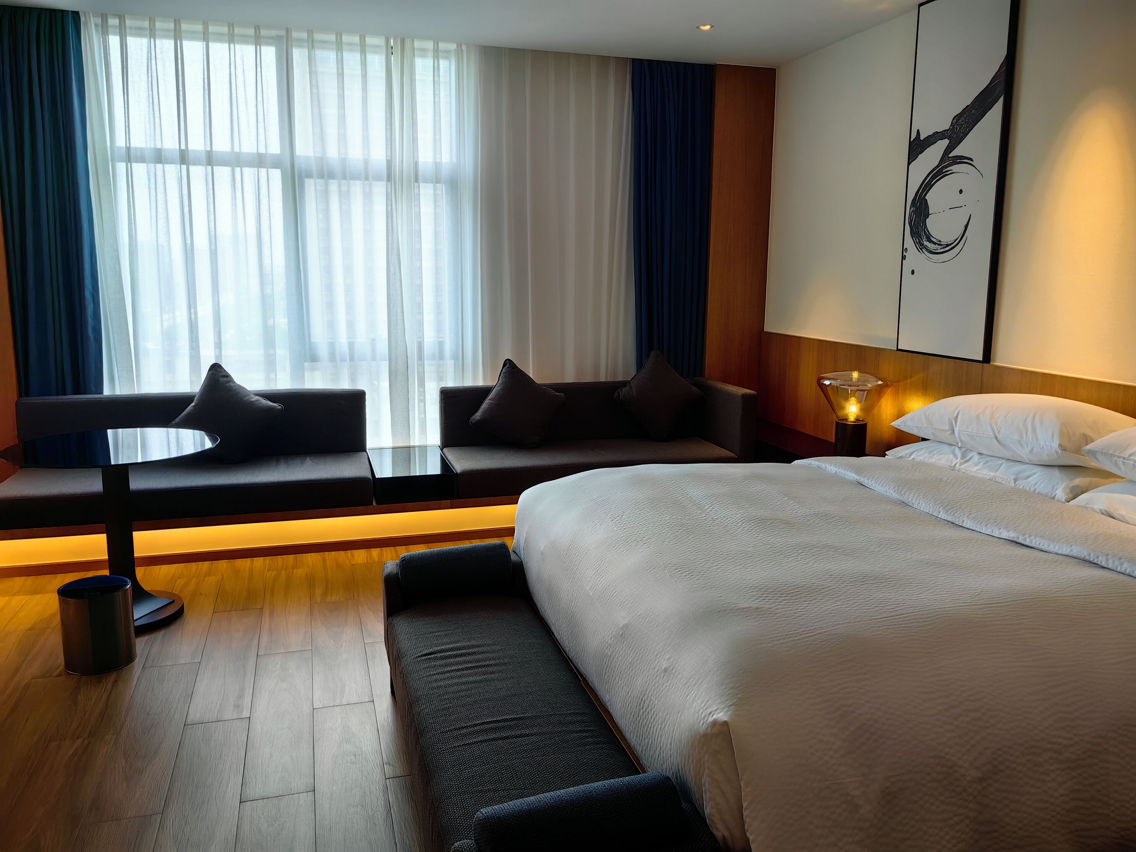 A hotel room with a large bed, a sofa, a small table, and a window with curtains.
