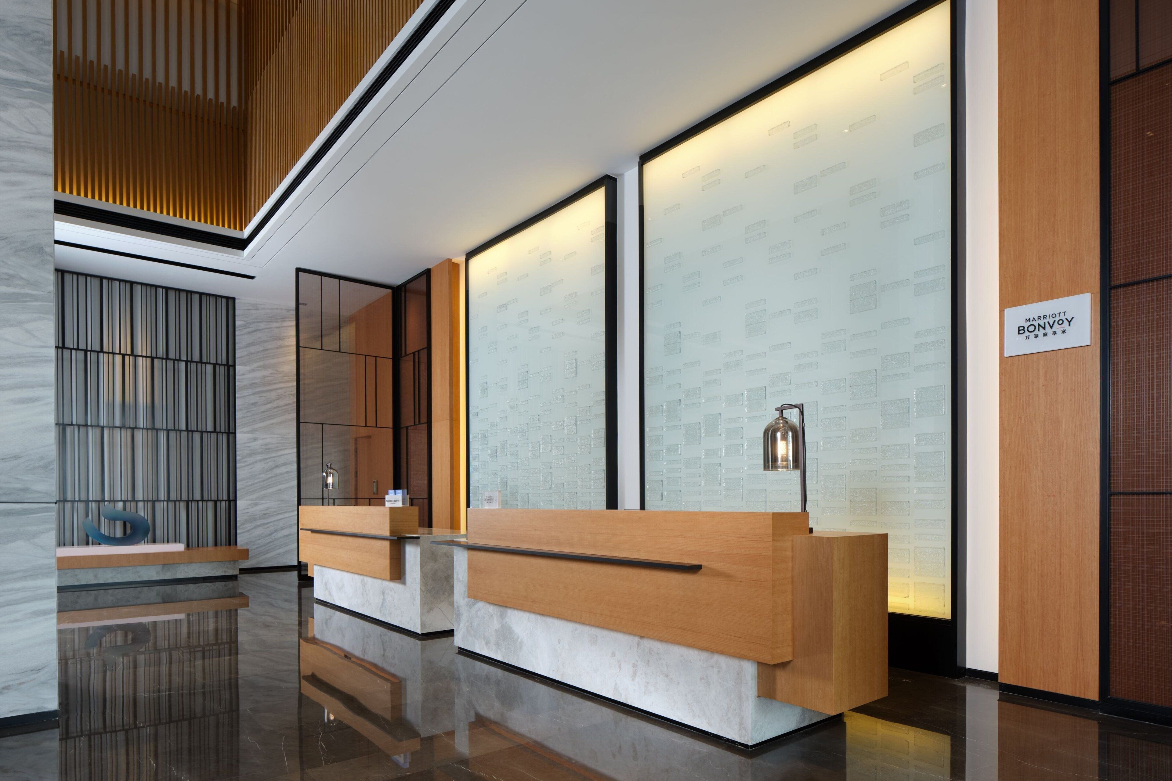 Un moderno mostrador de recepción con detalles de madera, un panel de vidrio y un letrero que indica 'Marriott Bonvoy'.