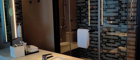 A modern bathroom with a large mirror, a white sink, a glass-enclosed shower, and a tiled wall.