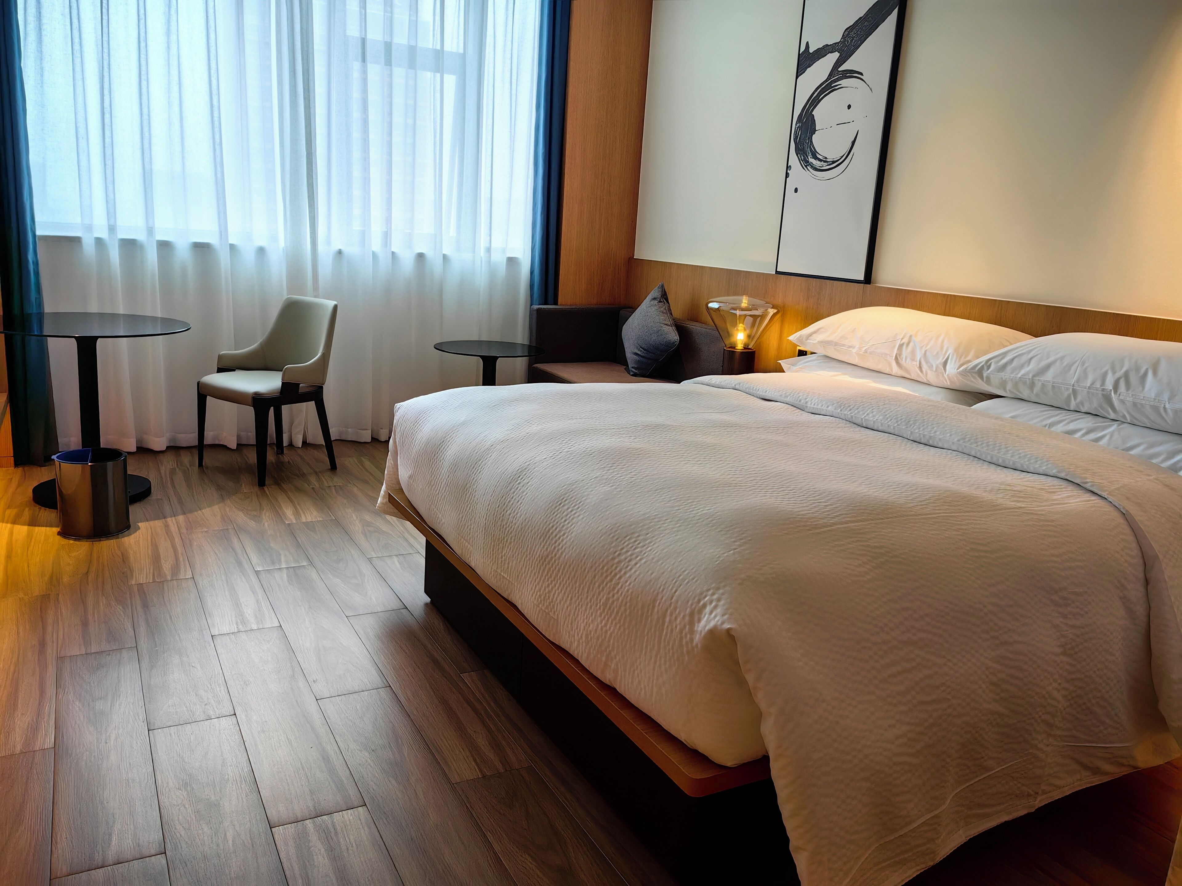 A hotel room with a large bed, a small table, a chair, and a lamp.