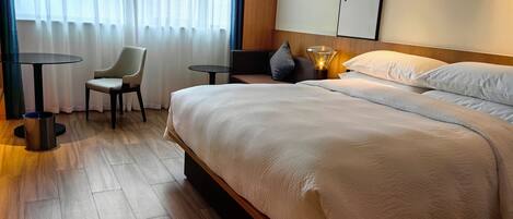 A hotel room with a large bed, a small table, a chair, and a lamp.