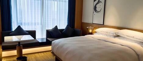 A modern hotel room with a large bed, a sofa with cushions, a small table, and a lamp.