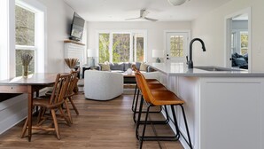 Une cuisine moderne avec un coin repas, des chaises en bois, un tabouret de bar et un téléviseur fixé au mur.