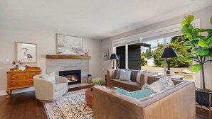 A modern living room with a fireplace, comfortable seating, and large windows offering a view of the outdoors.