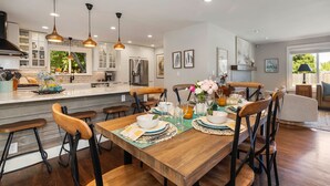 A modern kitchen with white cabinets, a wooden dining table set with plates, glasses, and a vase of flowers.
