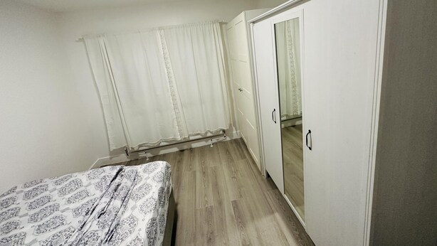 A bedroom with a bed, a wardrobe, a mirror, and a door leading to another room. - Immaculate 1-bed Apartment in Harrow (Harrow)