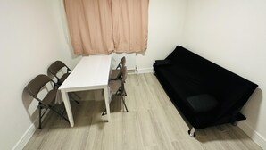 A small room with a white table and two chairs, a black sofa, and a window with beige curtains. - Immaculate 1-bed Apartment in Harrow (Harrow)