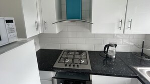 A kitchen with white cabinets, a black countertop, a gas stove, and a microwave. - Immaculate 1-bed Apartment in Harrow (Harrow)