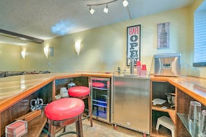 Zona de bar con taburetes, un refrigerador y un letrero que dice 'BAR OPEN'.
