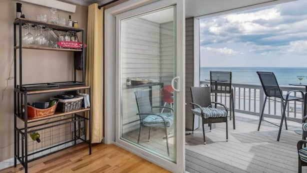 Ein Balkon mit Holzboden, einer Glastür und einem Tisch mit Stühlen.