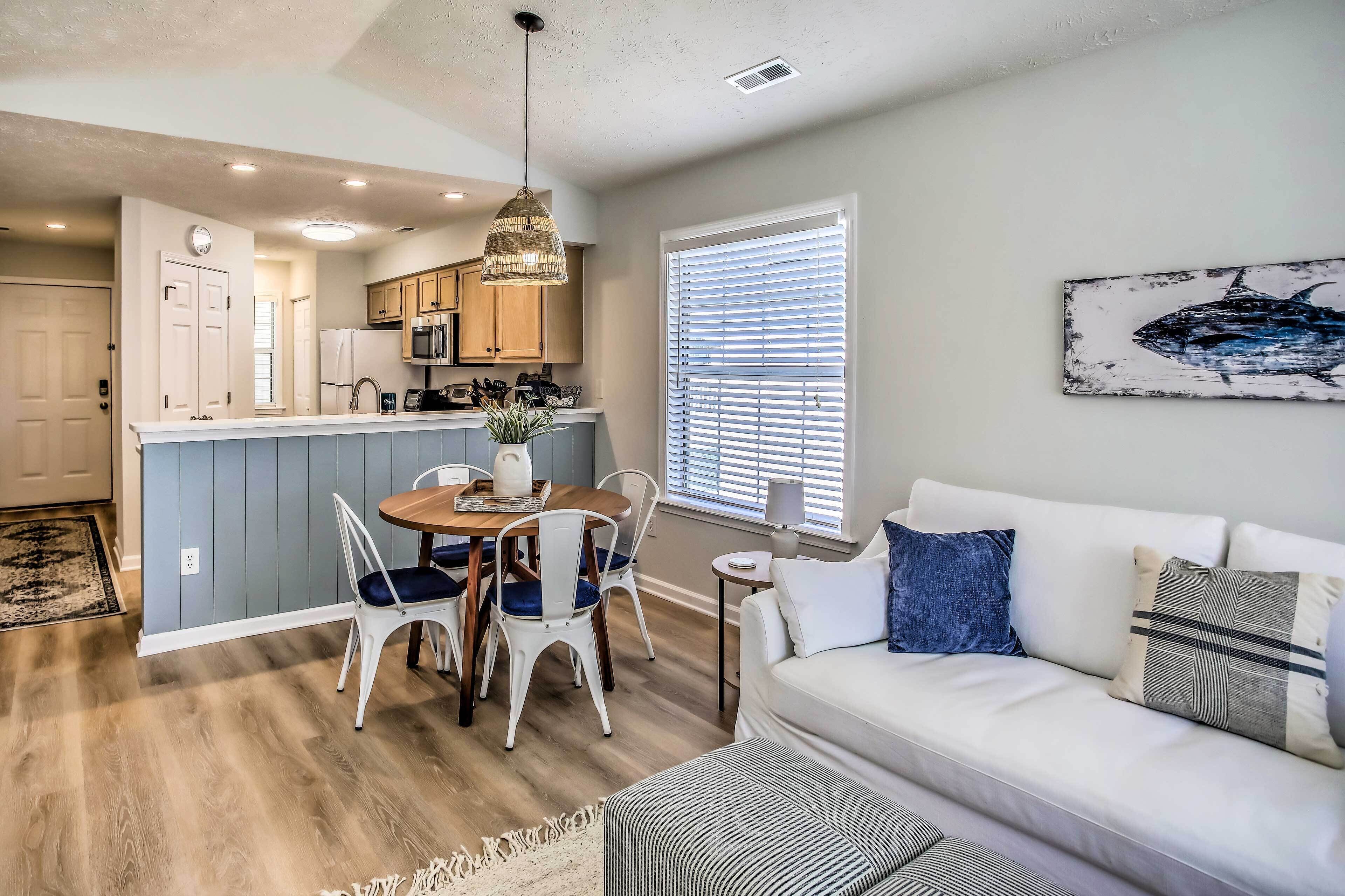 A modern kitchen with a dining area, a white sofa, and a large window with blinds.