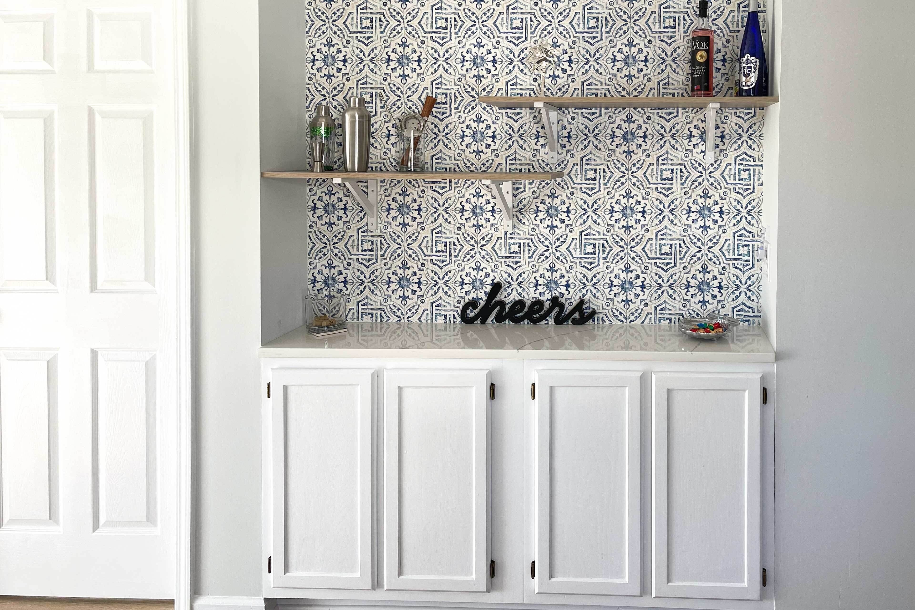 Eine Küche mit weißen Schränken, einer gemusterten Spritzschutzwand und einem Schild mit der Aufschrift 'cheers' auf der Arbeitsfläche.