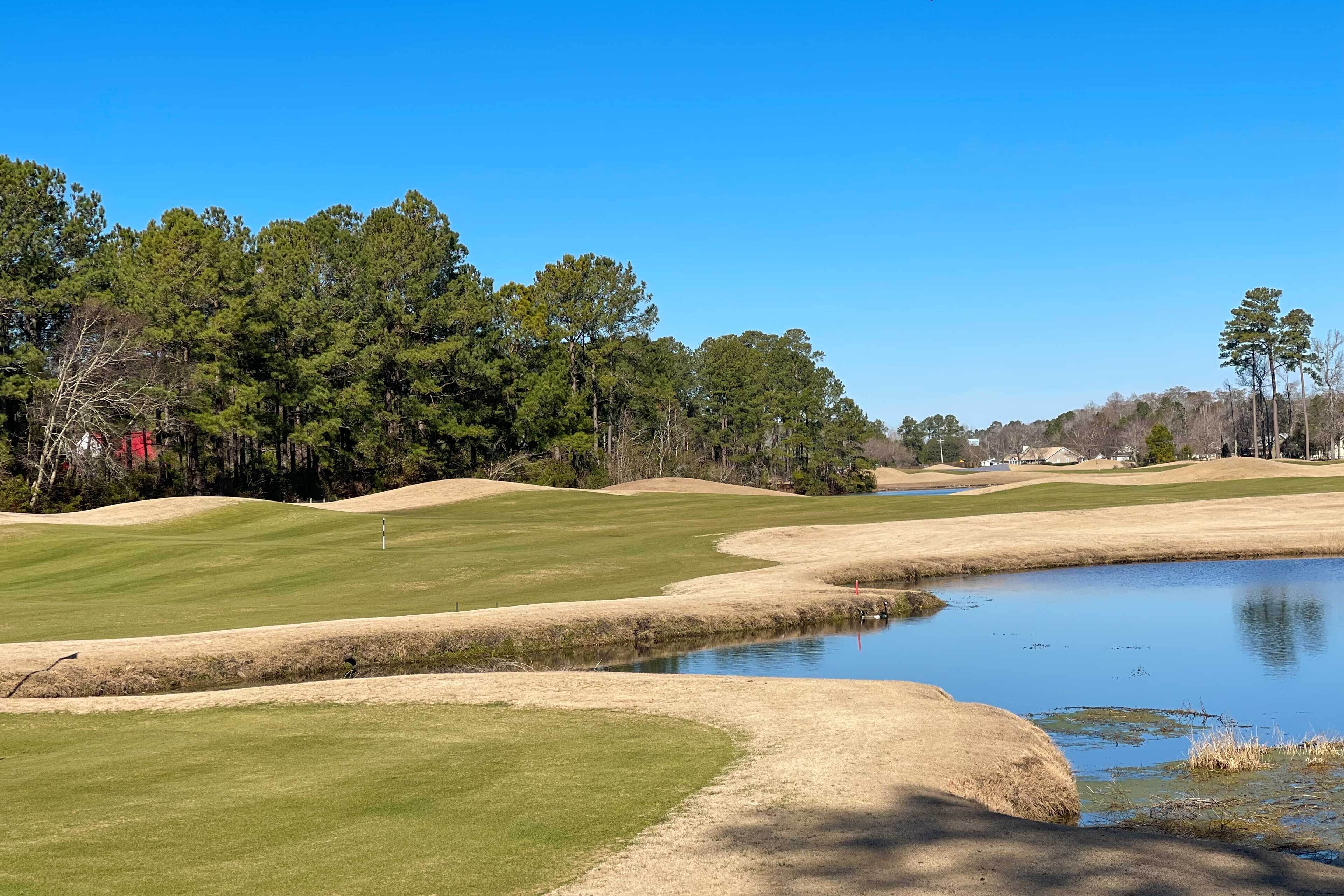 Ein Golfplatz mit Teich, umgeben von Bäumen und blauem Himmel.