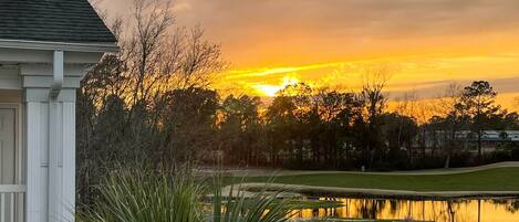 A house with a white exterior, a driveway, and a pond reflecting the sunset.