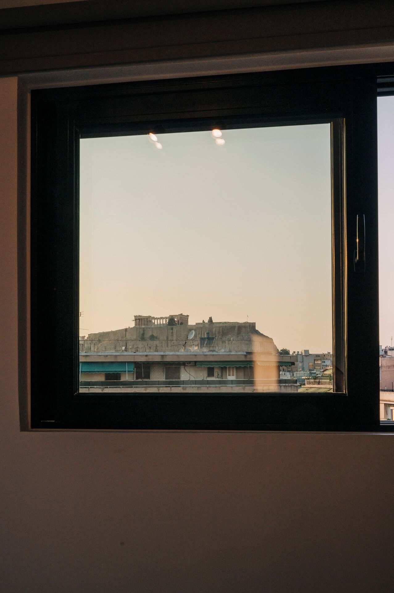 A window with a view of a building complex, including a large structure with multiple levels and a smaller building with a satellite dish.
