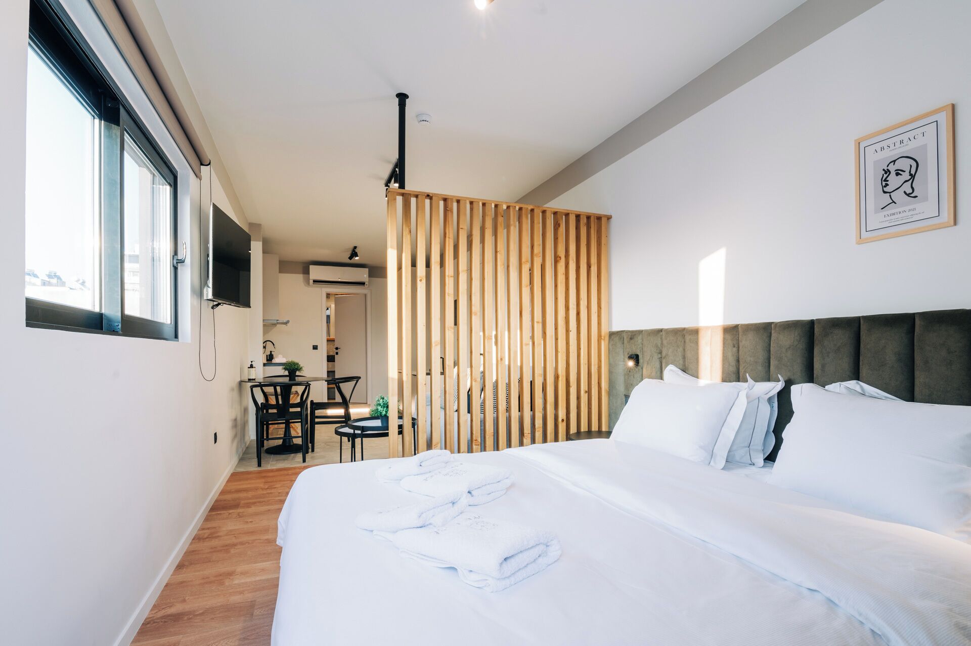 A modern hotel room with a large bed, a dining area, and a view of the city.
