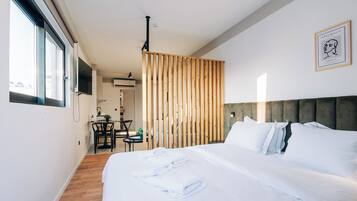 A modern hotel room with a large bed, a dining area, and a view of the city.