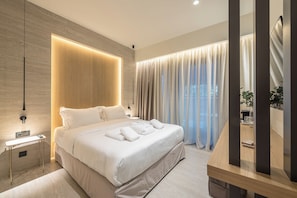 A modern hotel room with a large bed, bedside tables, a built-in light panel, and a view of the outdoors. - Athesense Suites (Athens)