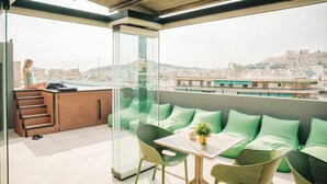 Un balcón con zona de estar, una pequeña mesa con una planta y vista a la ciudad.