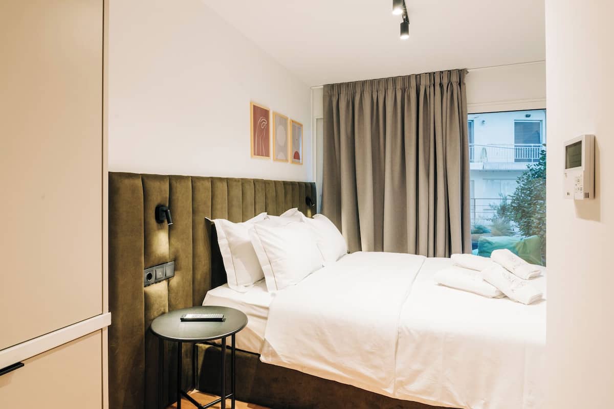 Una habitación de hotel con cama, una mesita, una lámpara de pared y una ventana con cortinas.