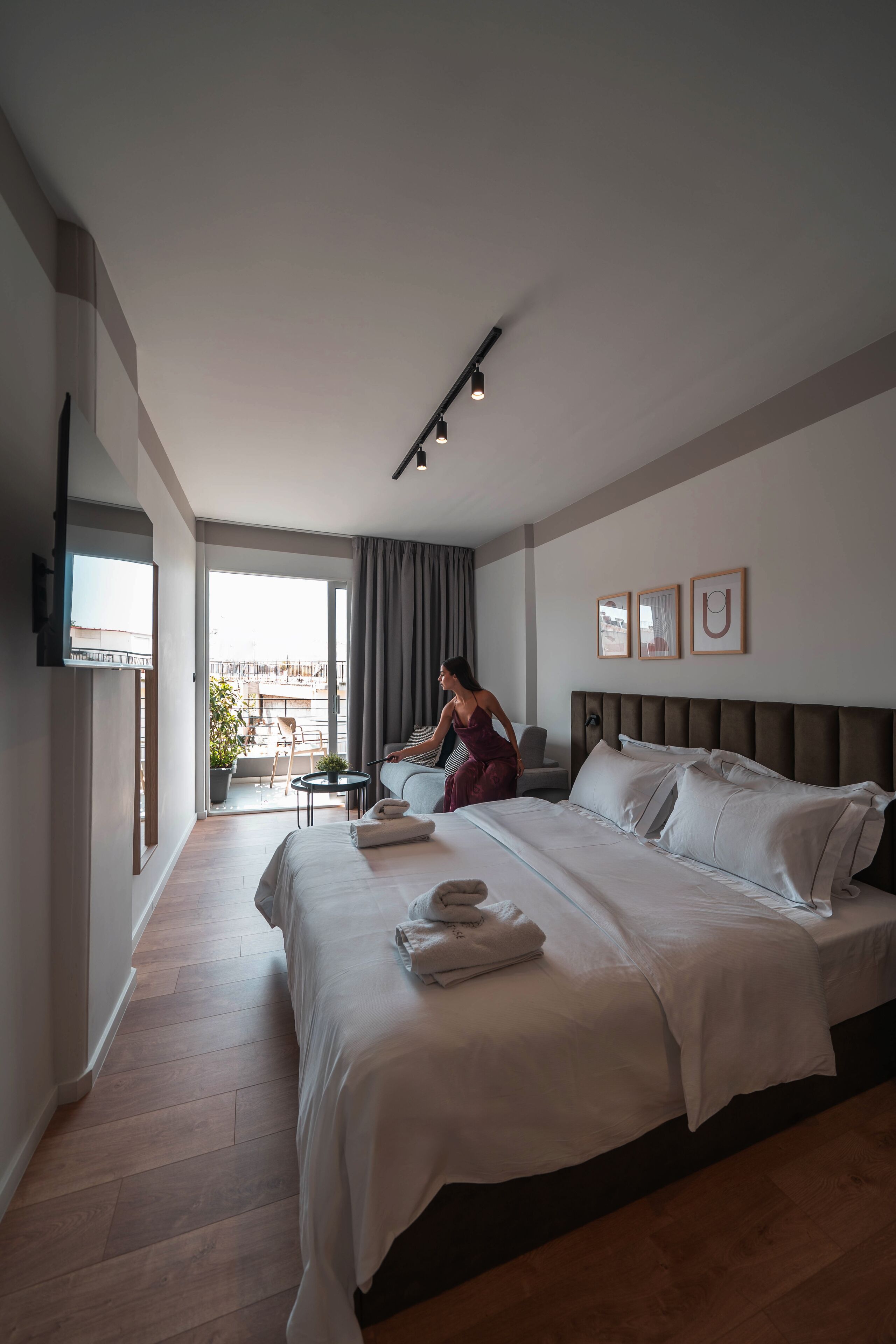 A hotel room with a large bed, a TV mounted on the wall, a balcony with a view, and a small table with a chair.