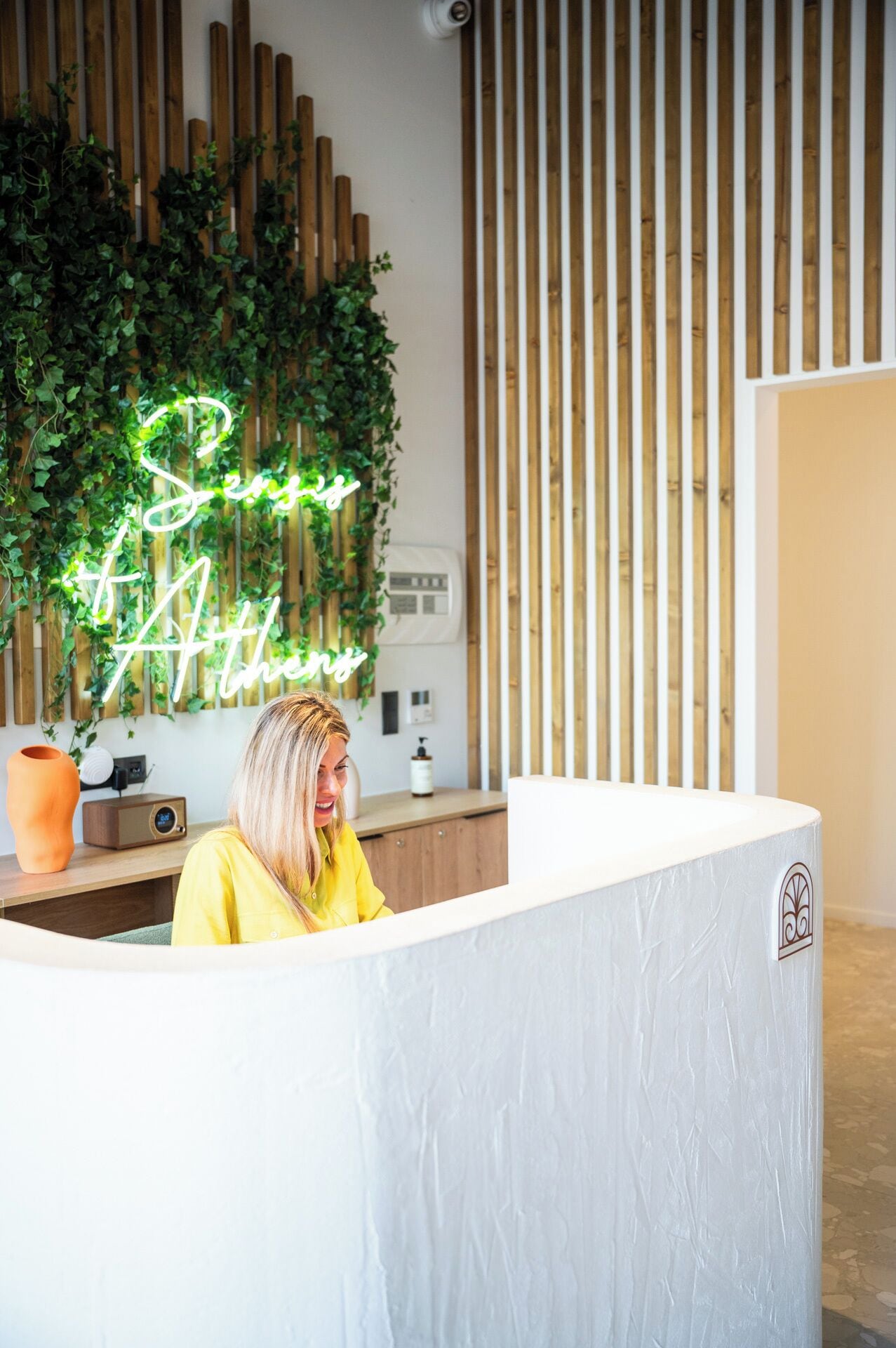 A reception desk with a neon sign reading "Sense & Style" and a wooden slat wall behind it.