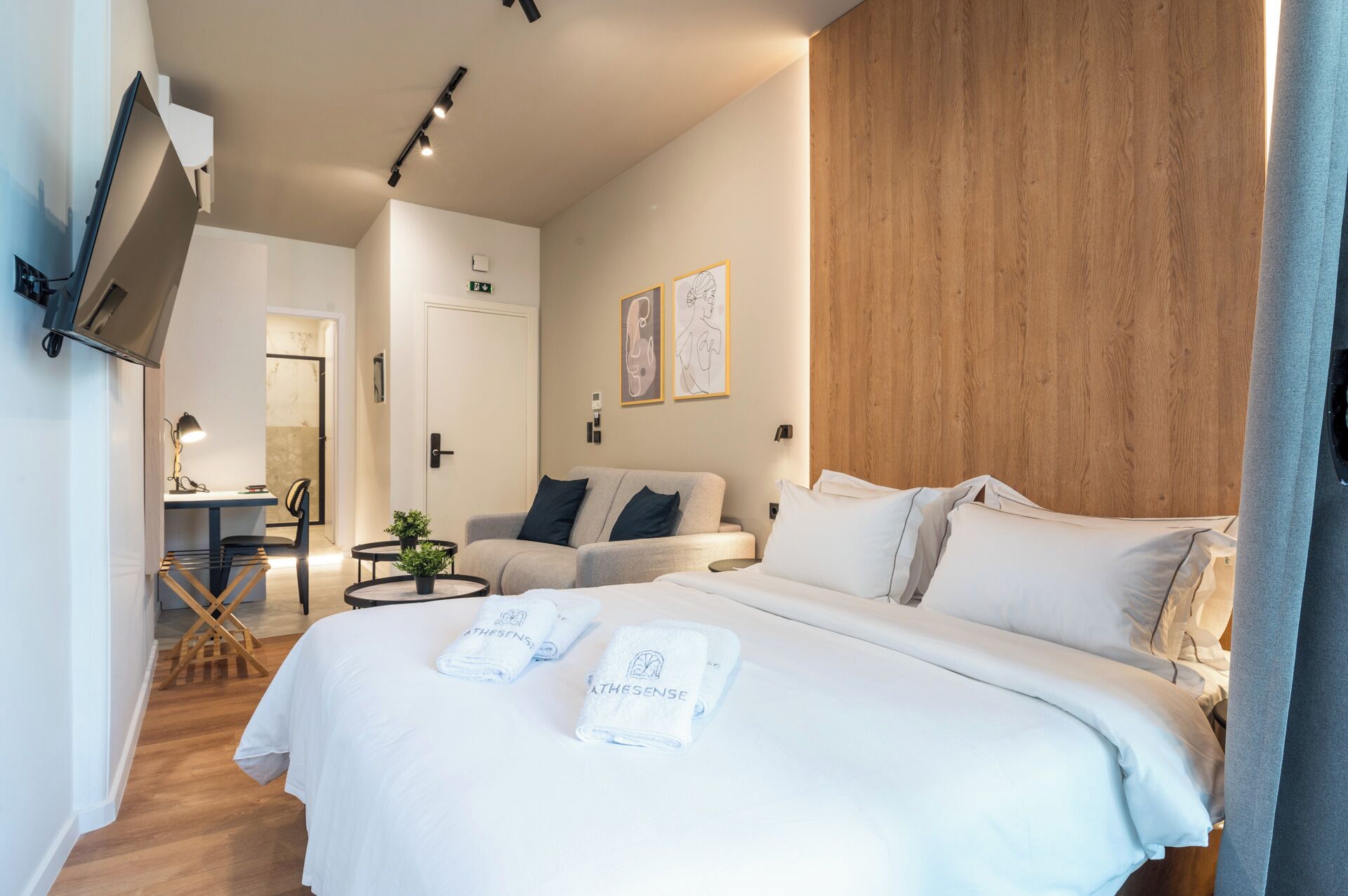 Ein Hotelzimmer mit einem großen Bett, einem Schreibtisch mit Stuhl, einem kleinen Tisch mit Pflanze und einer Wand mit Holzvertäfelung.