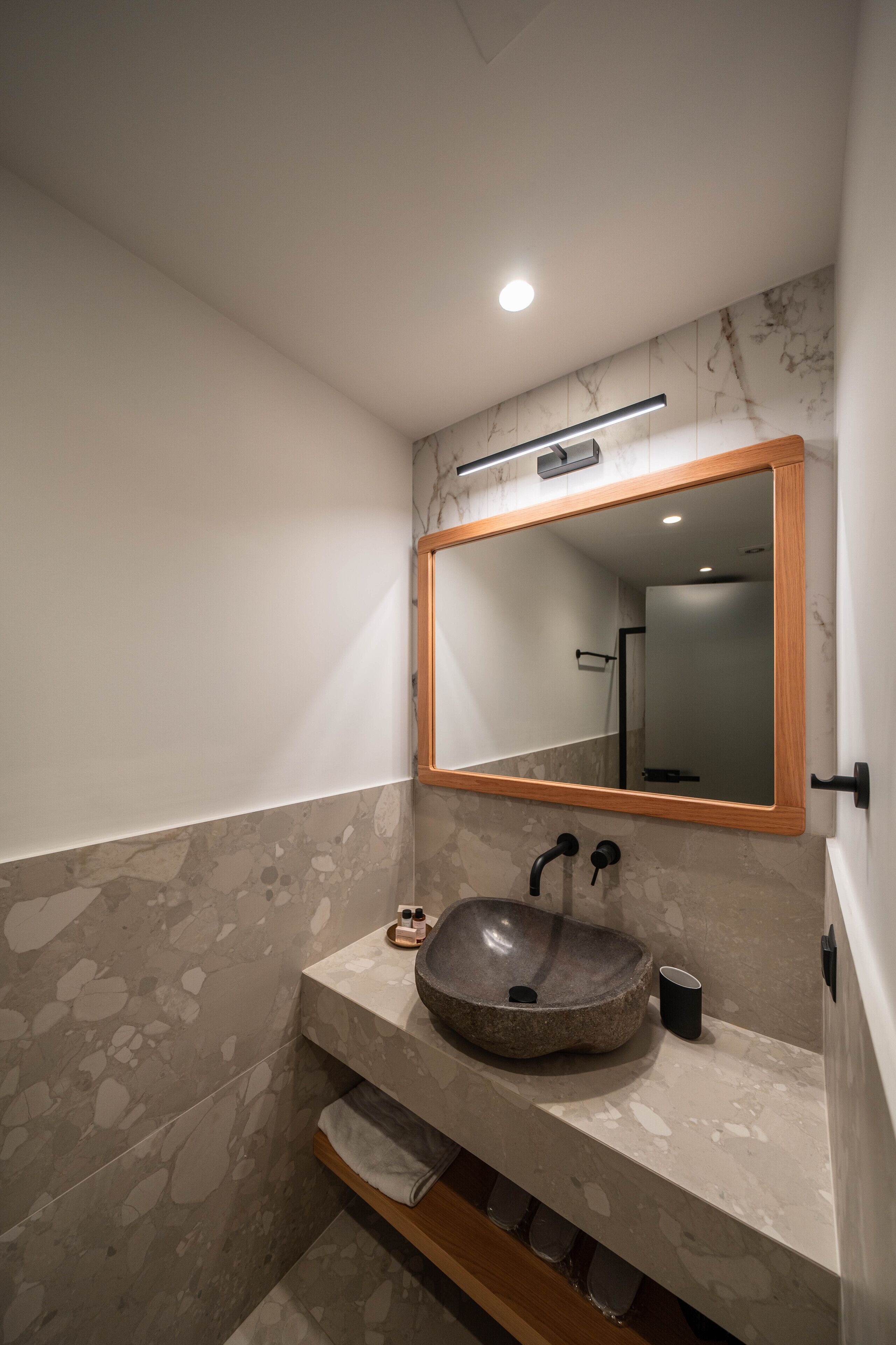 A bathroom with a stone sink, a wooden-framed mirror, and a marble wall.