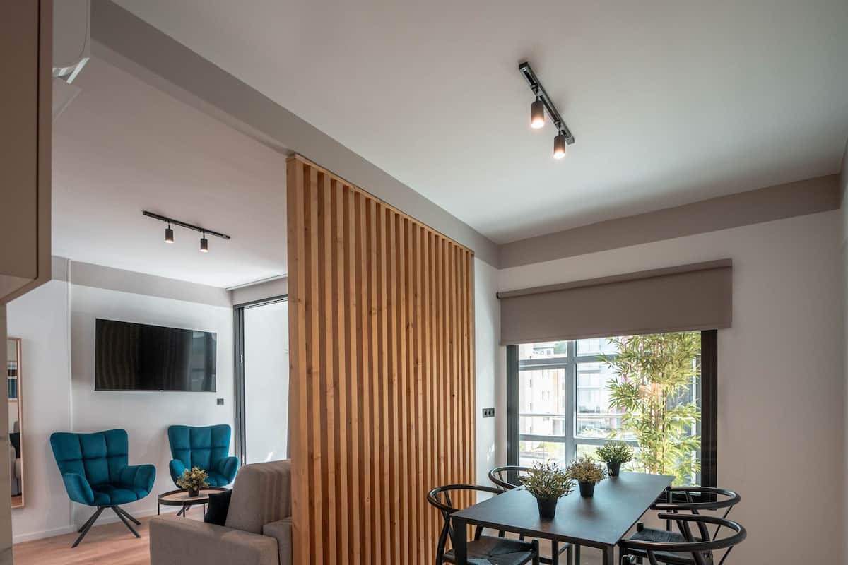 Una sala de estar moderna con comedor, televisor montado en la pared y un ventanal con vistas a edificios.