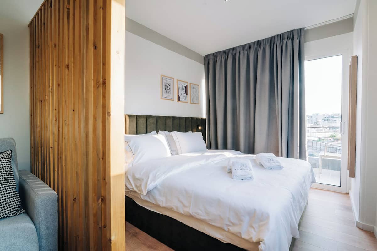 Una habitación de hotel moderna con una cama grande, un separador de madera y vistas a la ciudad.