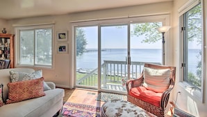 A living room with a sofa, a wicker chair, and a view of a lake through large sliding glass doors. - Luxe Chesapeake Bay Getaway < 20 Mi to Annapolis! (Shady Side)