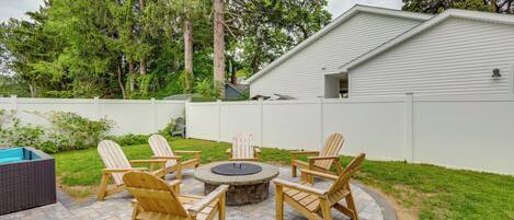 A backyard with a circular fire pit table surrounded by wooden Adirondack chairs.