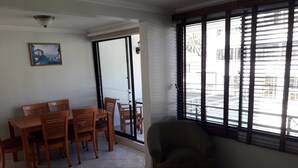 A dining area with a table and chairs, a sofa, and a window with blinds. - Habitamar Maitencillo (Puchuncavi)