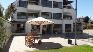A modern two-story building with a patio area featuring outdoor furniture and a large umbrella. - Habitamar Maitencillo (Puchuncavi)