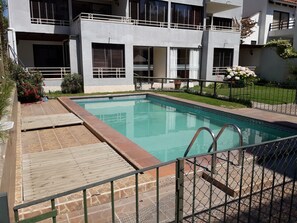 A swimming pool with a wooden deck and metal railing, surrounded by a fence. - Habitamar Maitencillo (Puchuncavi)