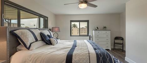 A bedroom with a bed, a ceiling fan, a dresser, and a window.