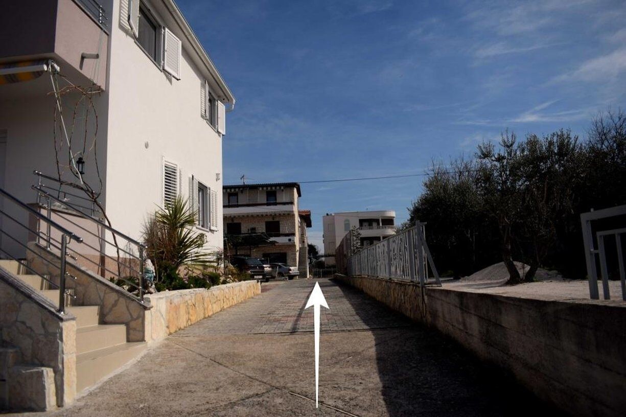 A narrow urban street with a clear directional arrow on the pavement, flanked by residential buildings and a stone wall on one side.